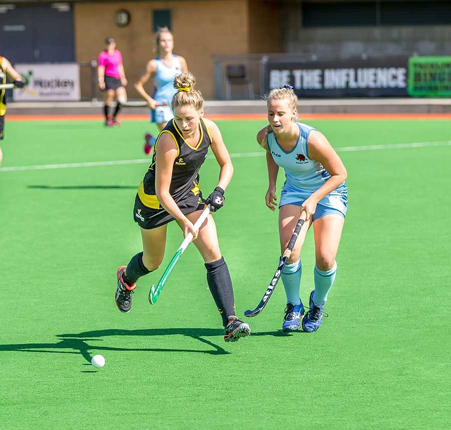 Two young women on opposing hockey teams vie for the ball.