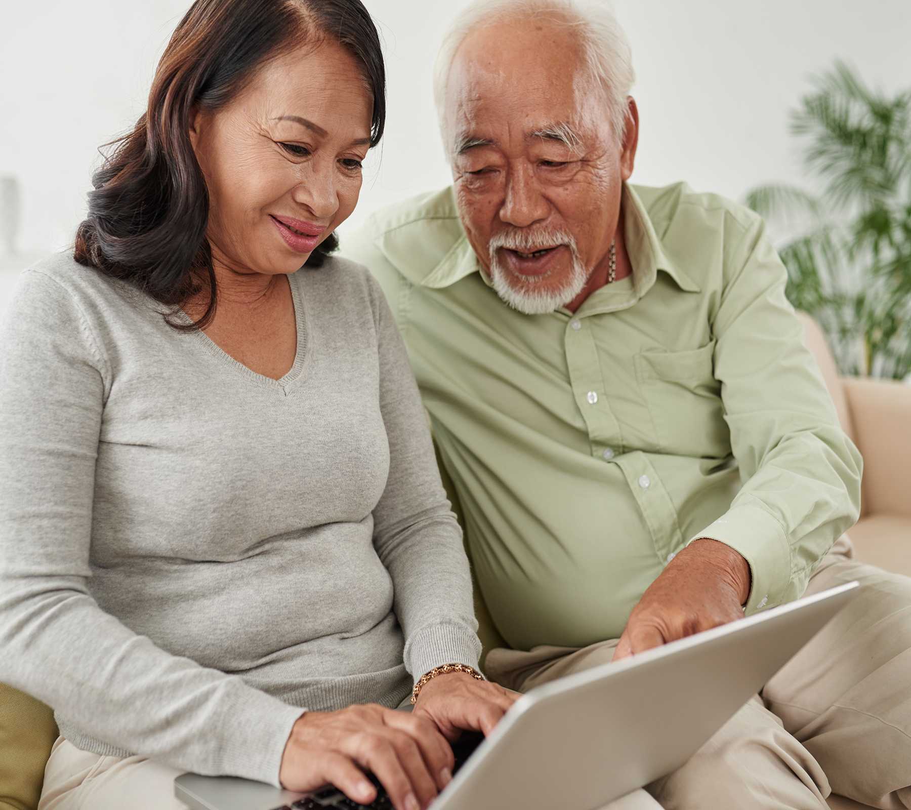 An older Vietnamese couple work together on a laptop.