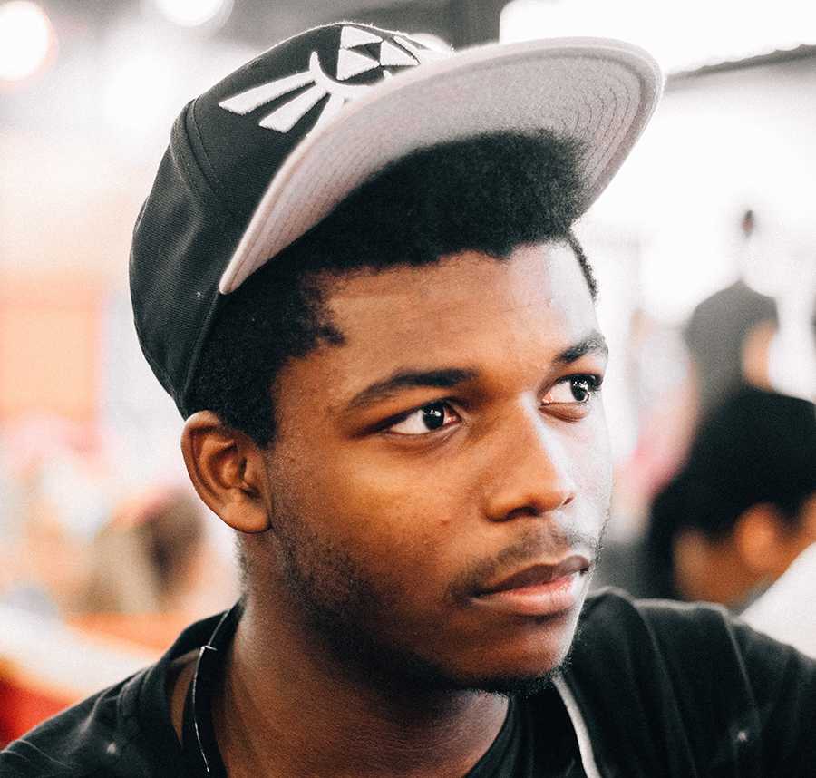 A young black man in a cap stares into the distance