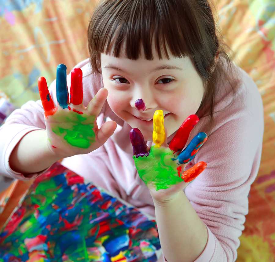 A young girl with Down Syndrome smiles as she shows off her hand painting.