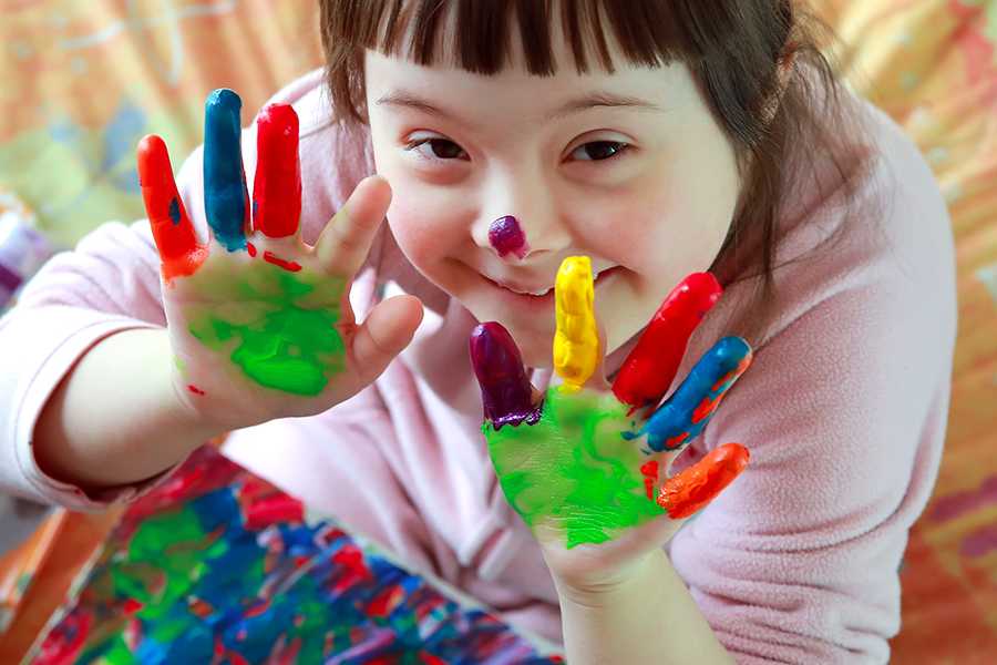 A young girl with Down Syndrome smiles as she shows off her hand painting.