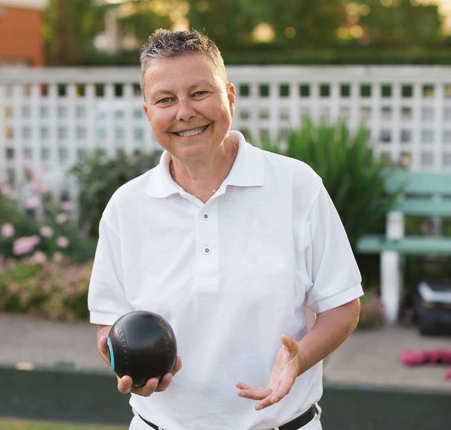 An older woman smiles in a clean white shirt at a Bowls Club.
