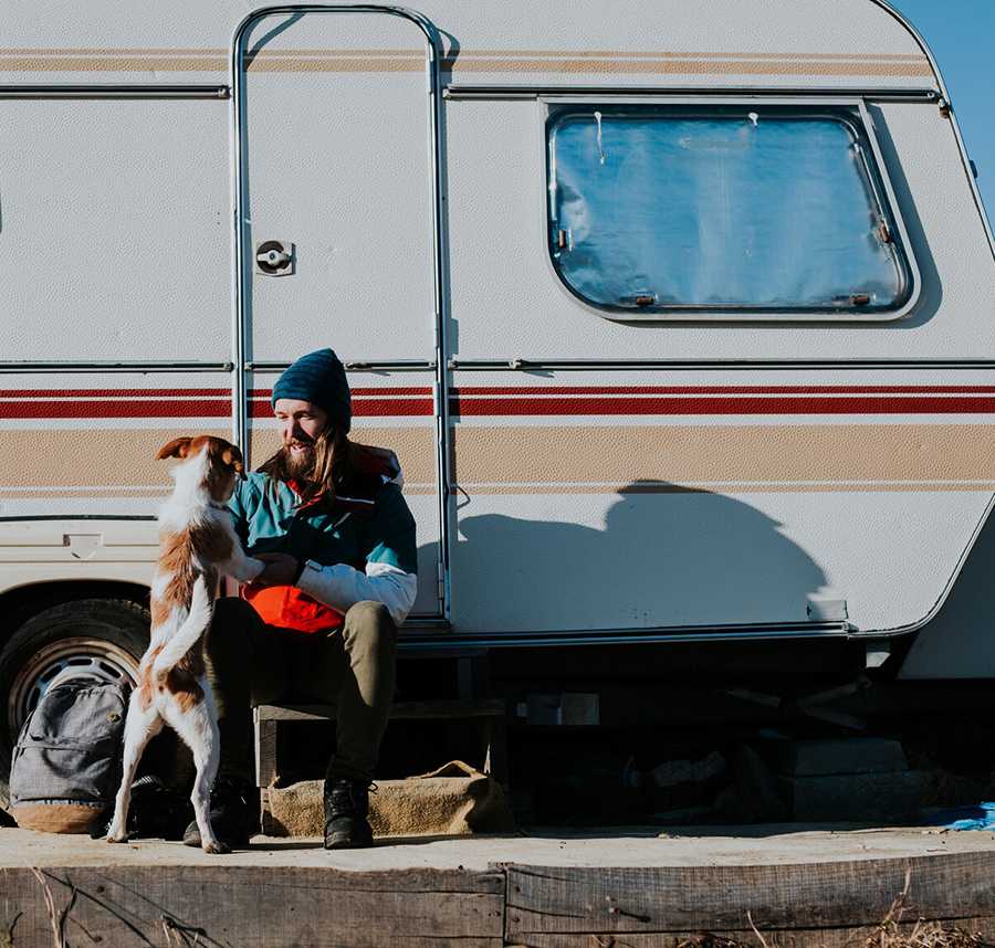 A man and his dog play together outside their caravan.