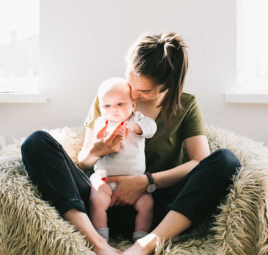 A mother sits on a beanbag with her newborn baby in her lap.