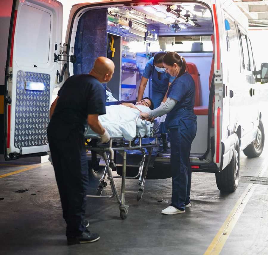 Paramedics wheel a patient from the back of an ambulance.