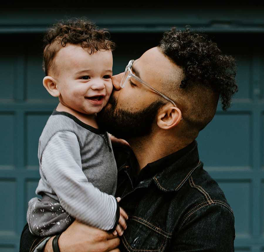 A father lovingly kisses his young son who has a similar hairstyle to him.