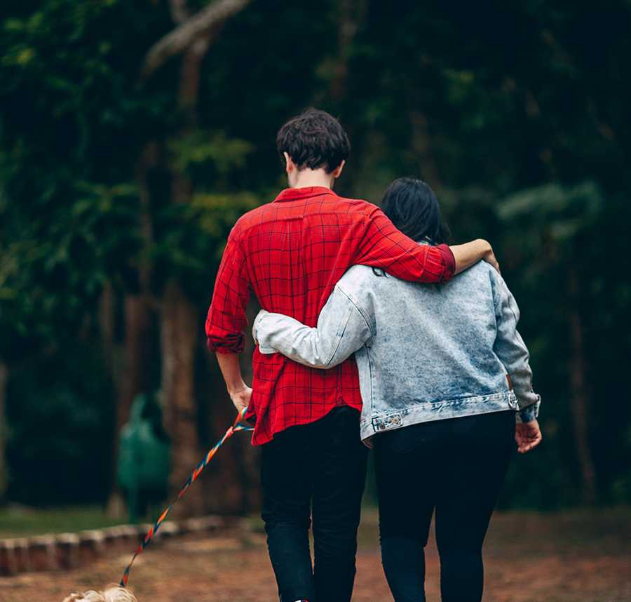 A man and woman walk their dog with their arms wrapped around each other.
