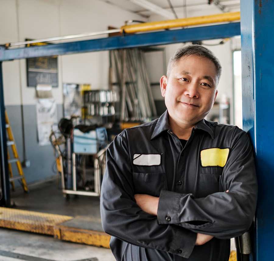 A middle-age man in work gear leans against a pole in a workshop.