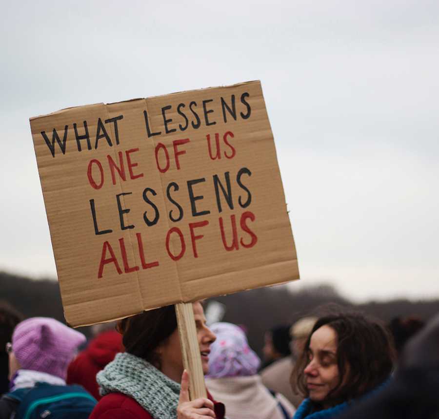 A protester holds a sign which reads: "What lessens one of us, lessens all of us."