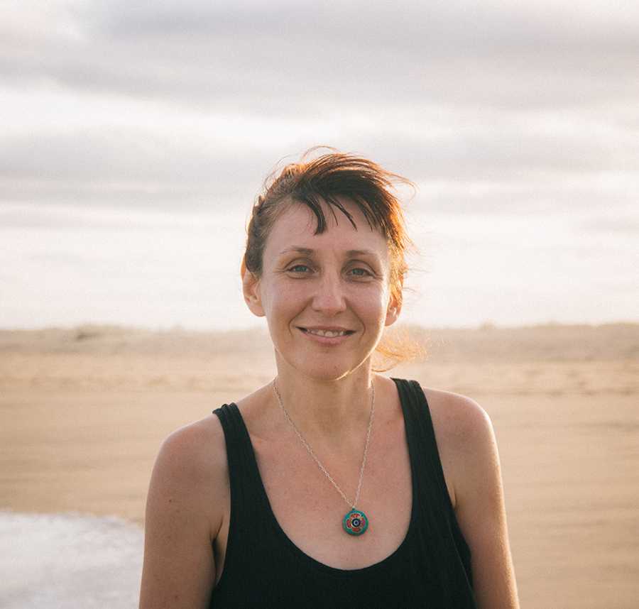 A white middle-aged woman with a fringe stands on the beach smiling