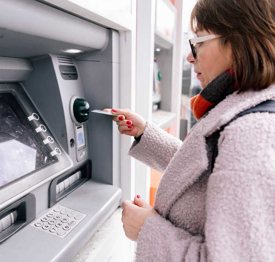 A middle-aged woman in a coat places her card into an ATM.