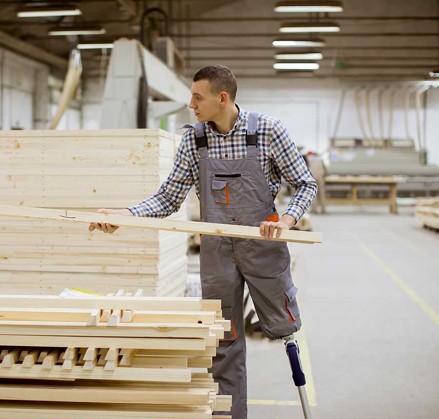 A factory worker with a prosthetic limb picks up a plank of wood.