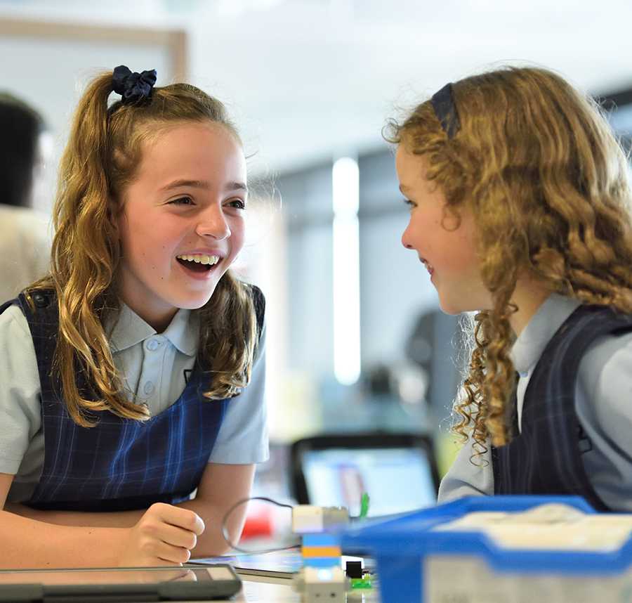 Two young schoolgirls laugh together.