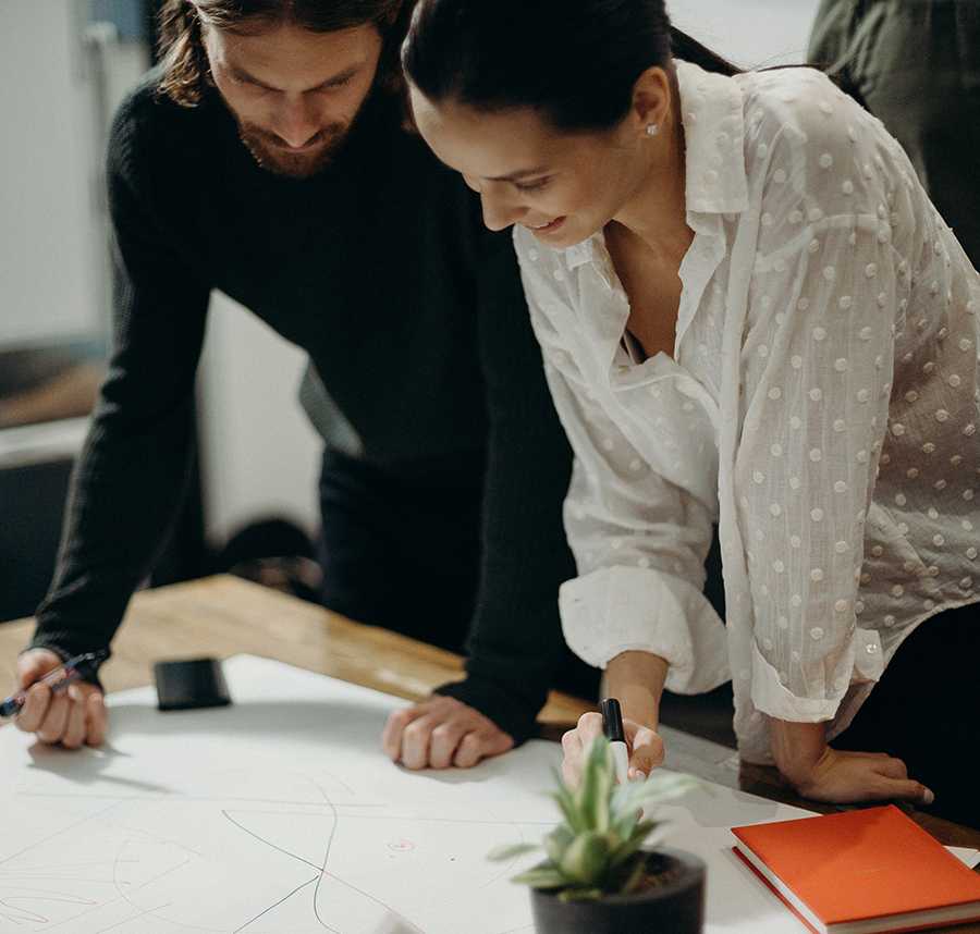 A man and a woman in business attire lean over a diagram on the table.