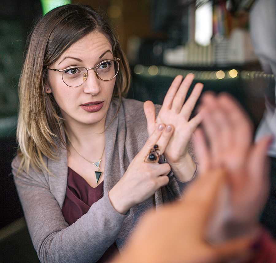 Two young women sit at a cafe communicating through Auslan.