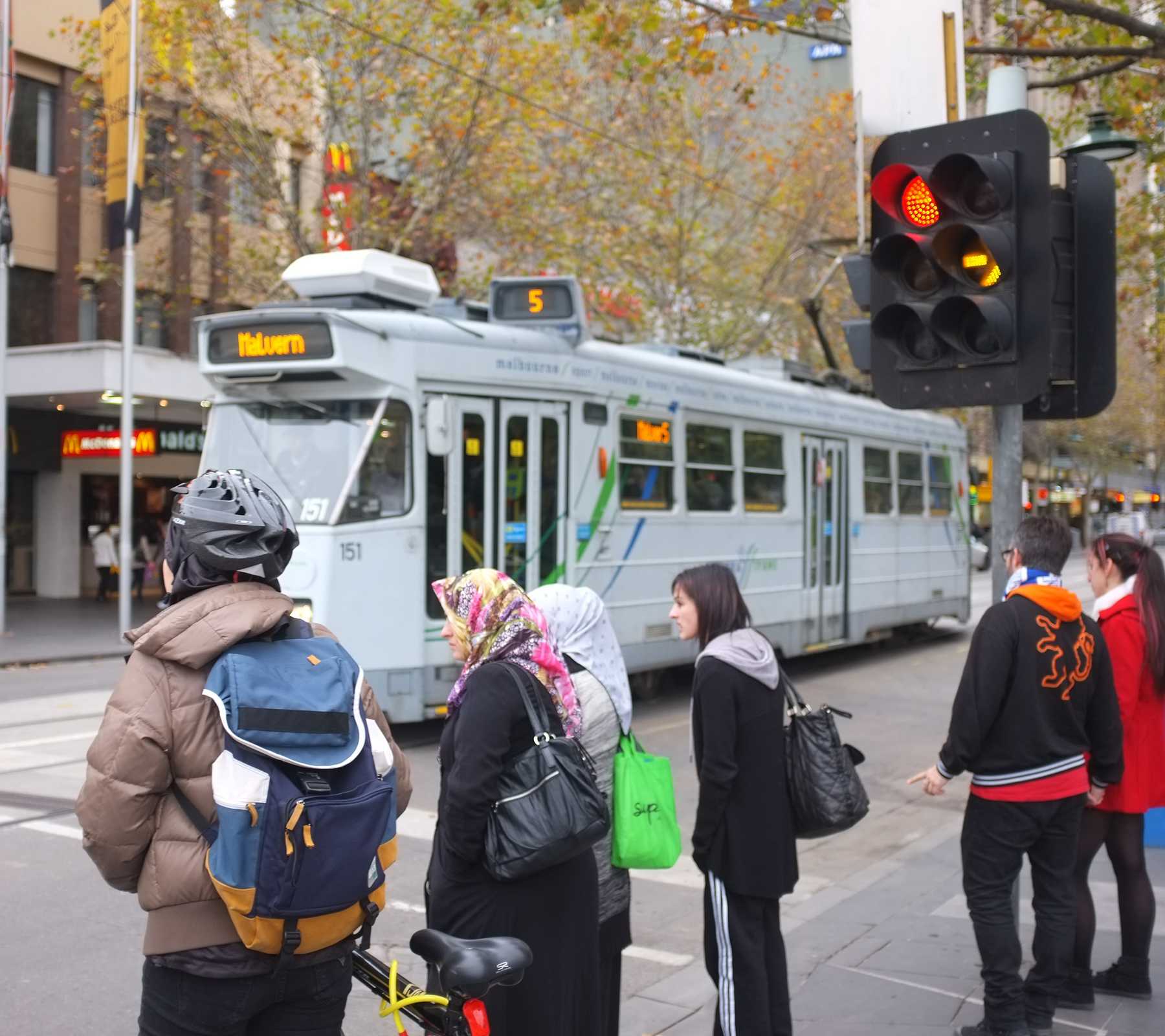 Tram passing pedestrians on a Melbourne city street.