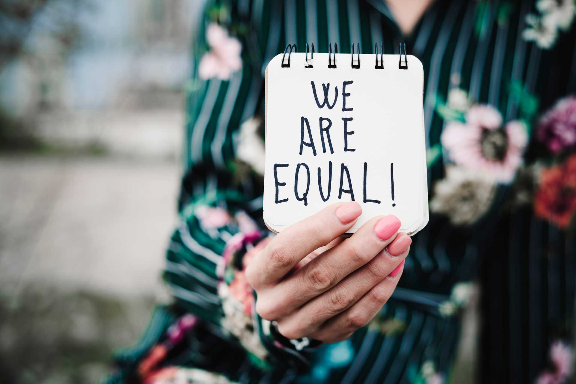 closeup of a young woman outdoors showing a notepad in front of her with the text we are equal written in it